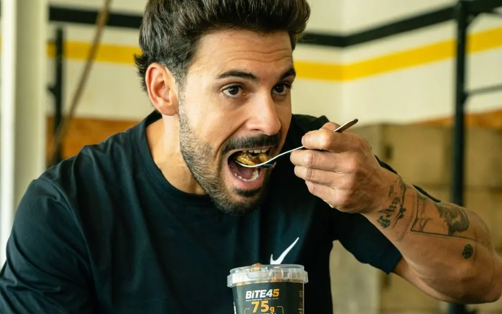 Athlete taking a big bite of a BITE45 protein pack in the gym